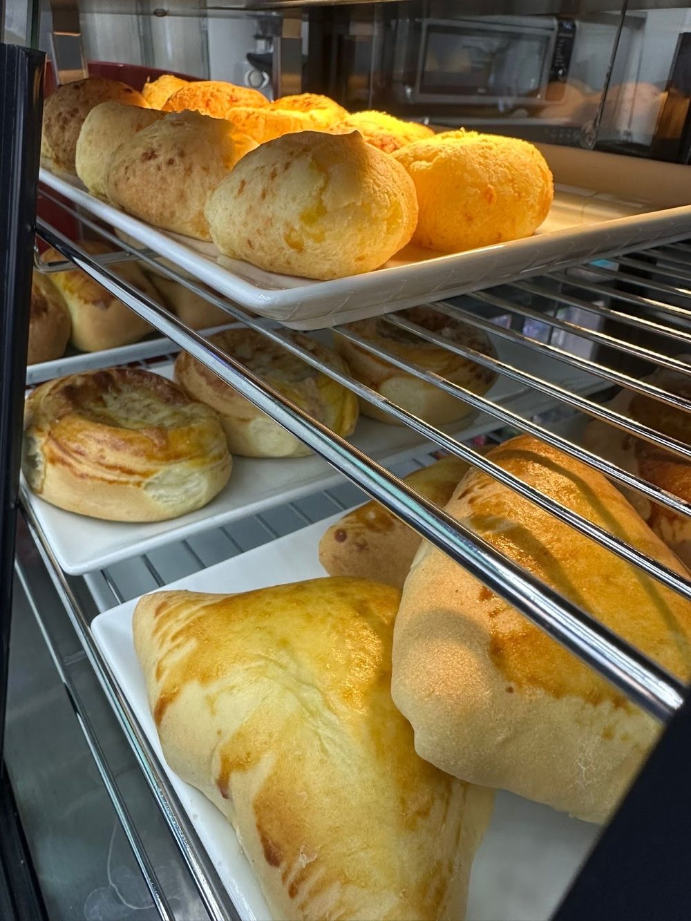 Trays of freshly baked bread rolls and pastries on wire racks inside the counter display