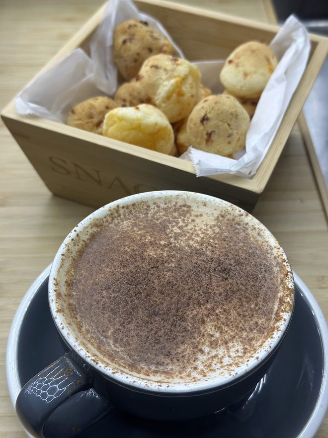 A cappuccino with latte art held at the counter, the fridges and cafe soft behind