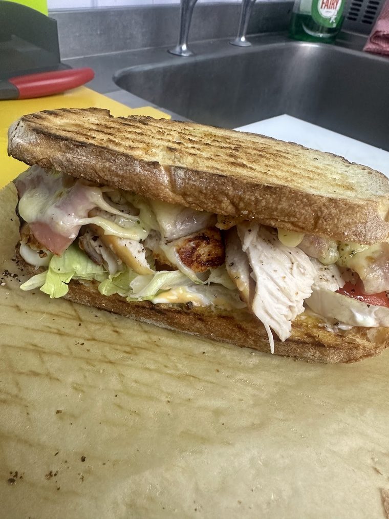 A toasted pressed sandwich with roast chicken, ham, melted cheese and lettuce, cut open on parchment